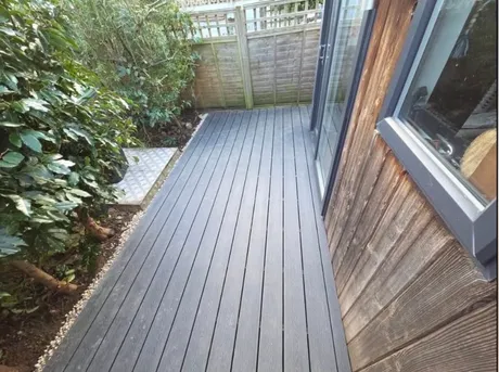 Composite decking laid up to the doors of a timber clad garden room, with a gravel margin along the edge.