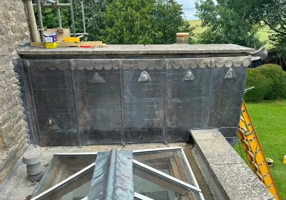 A dormer clad in lead with welted seams, a scalloped lower edge and cast lead ornaments, above a glazed lantern.