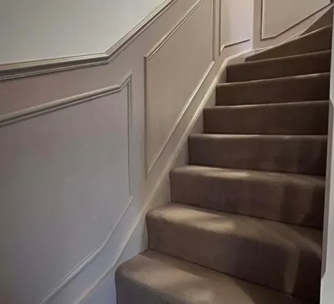Moulded panelling run up a staircase wall, following the rake of the stairs, with a cap rail along the top.